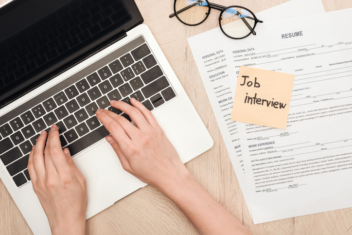 cropped view of recruiter typing on laptop keyboard near glasses, resume templates and sticky note with job interview lettering