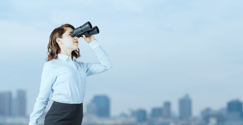 Young businesswoman using binoculars in front of the city skyline